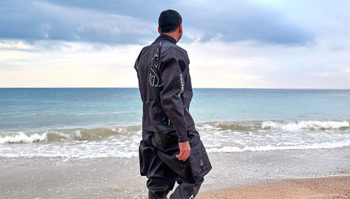 Man walking in the surf wearing a SCUBAPRO Definition Dry HD Drysuit