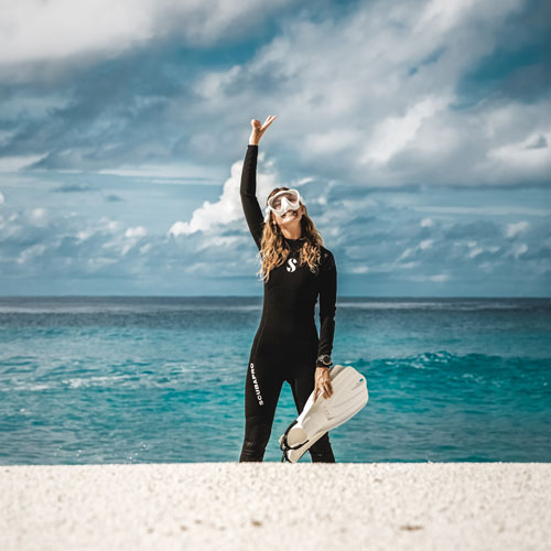 Woman in a white mask carrying fins on the beach