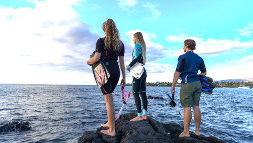 Three snorkelers in SCUBAPRO divewear standing on a rocky shore