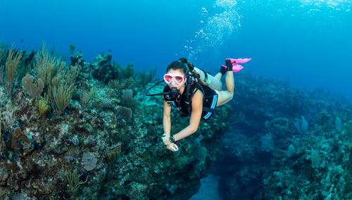 Woman diver in a SCUBAPRO GO BCD swimming over coral reefs