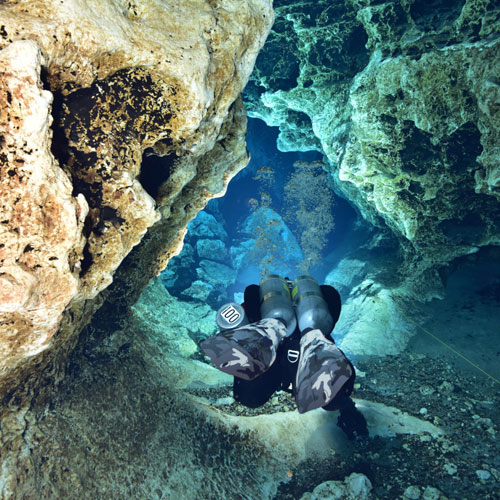 Diver underwater swimming through a rock cave