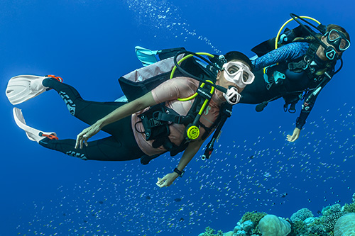 Two scuba divers using C70 in white and turquoise color frames underwater over a coral reef