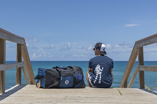 Person sitting on a wooden dock facing the ocean with Sport Mesh 'N Roll 100