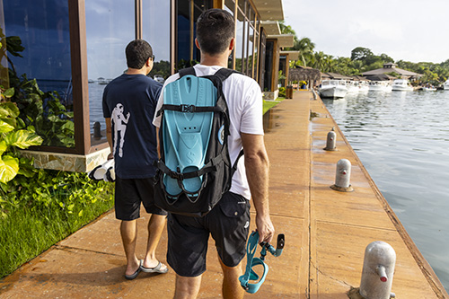 Person carrying snorkeling gear along a marina walkway.