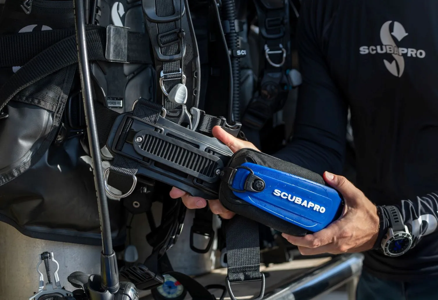 Close-up of a diver attaching a blue SCUBAPRO Hydros Pro 2 Monorail Weight Pocket to a Hydros Pro 2 BCD, showing the integrated monorail weight system and secure attachment mechanism.