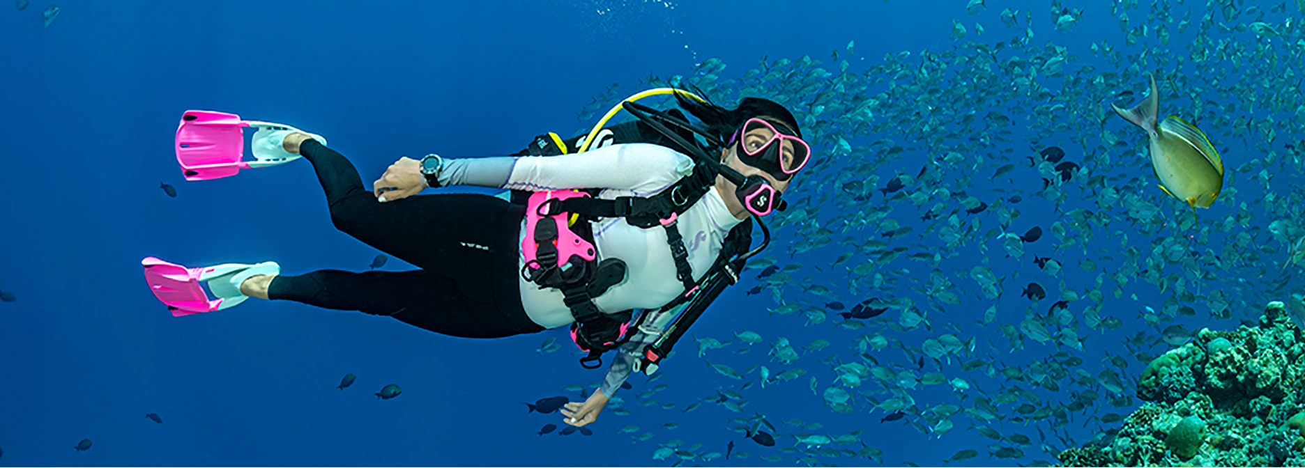 Scuba diver exploring a coral reef while surrounded by a school of fish during a test dive experience.