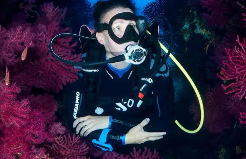 Diver using  MK25 EVO/S620 Ti White Scuba Regulator swimming among vibrant pink and red coral formations